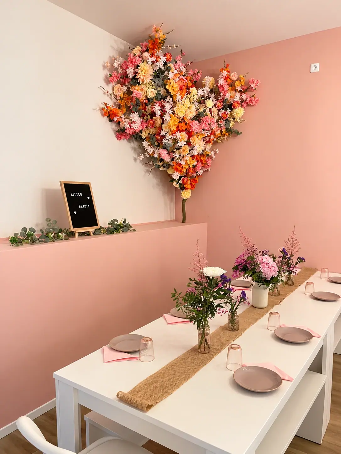 Gedeckter Tisch mit Wiesenblumen, Blumenwand in der Ecke und Letterboard für einen Kindergeburtstag