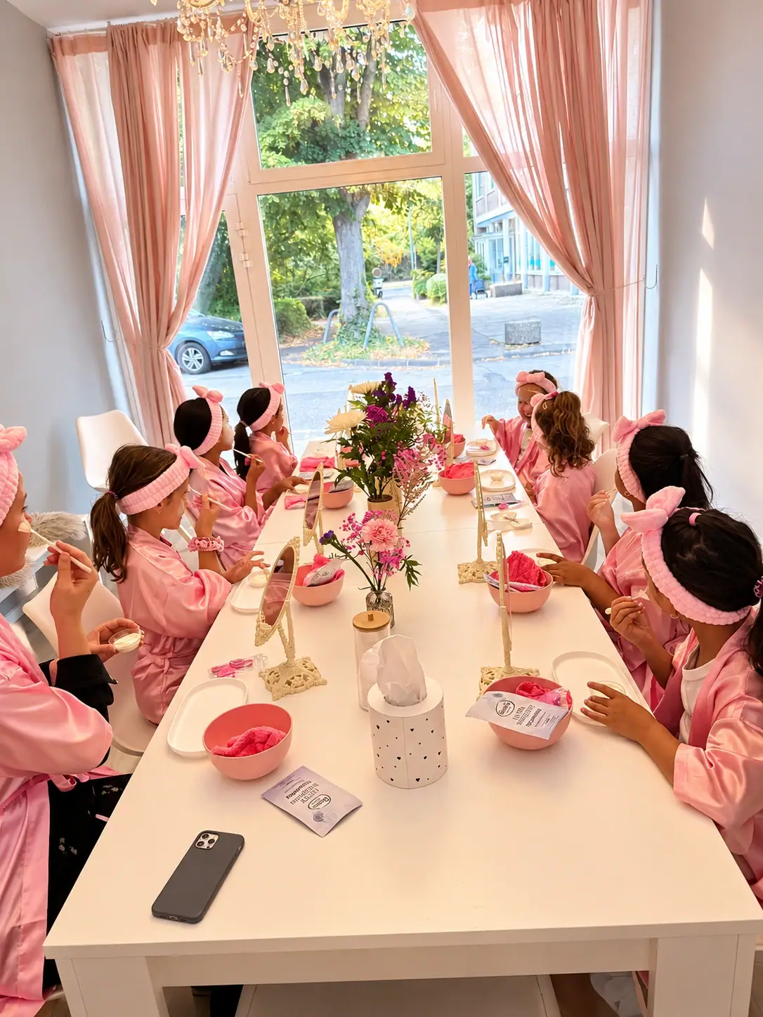 Mädchen tragen beim Face-Spa ihre Gesichtscreme auf, am Spa-Tisch vor dem großen Fenster mit rosa Vorhängen