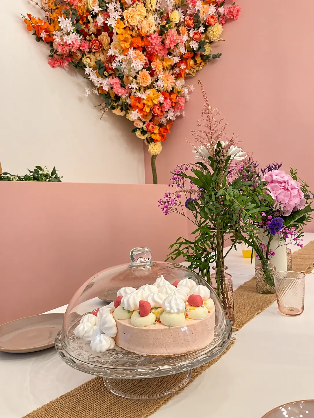 Geburtstagstorte mit Baiser und Erdbeeren unter einer Glashaube vor der Blumenwand