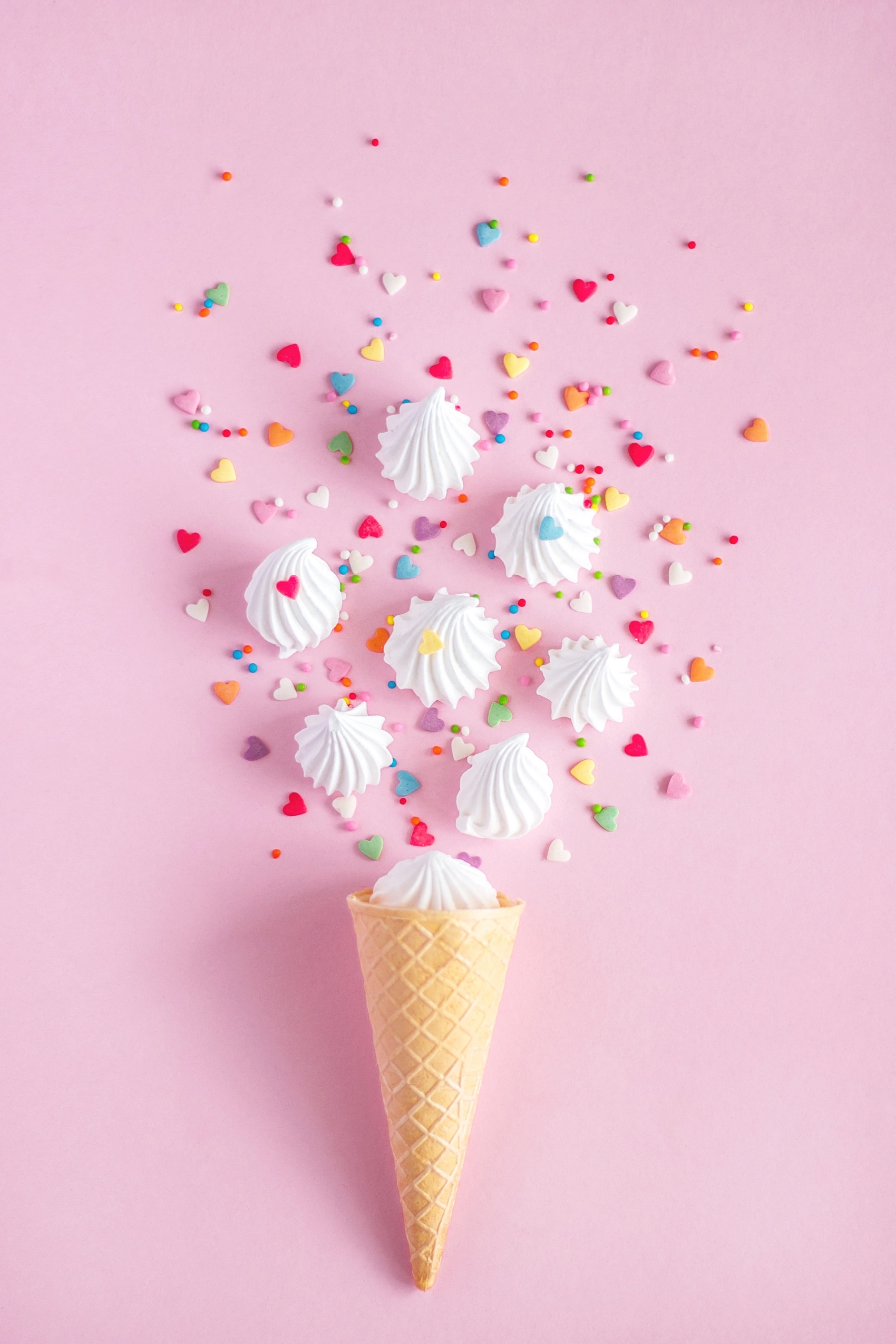 Eiswaffel mit Baiser und bunten Zuckerherzen auf rosa Hintergrund