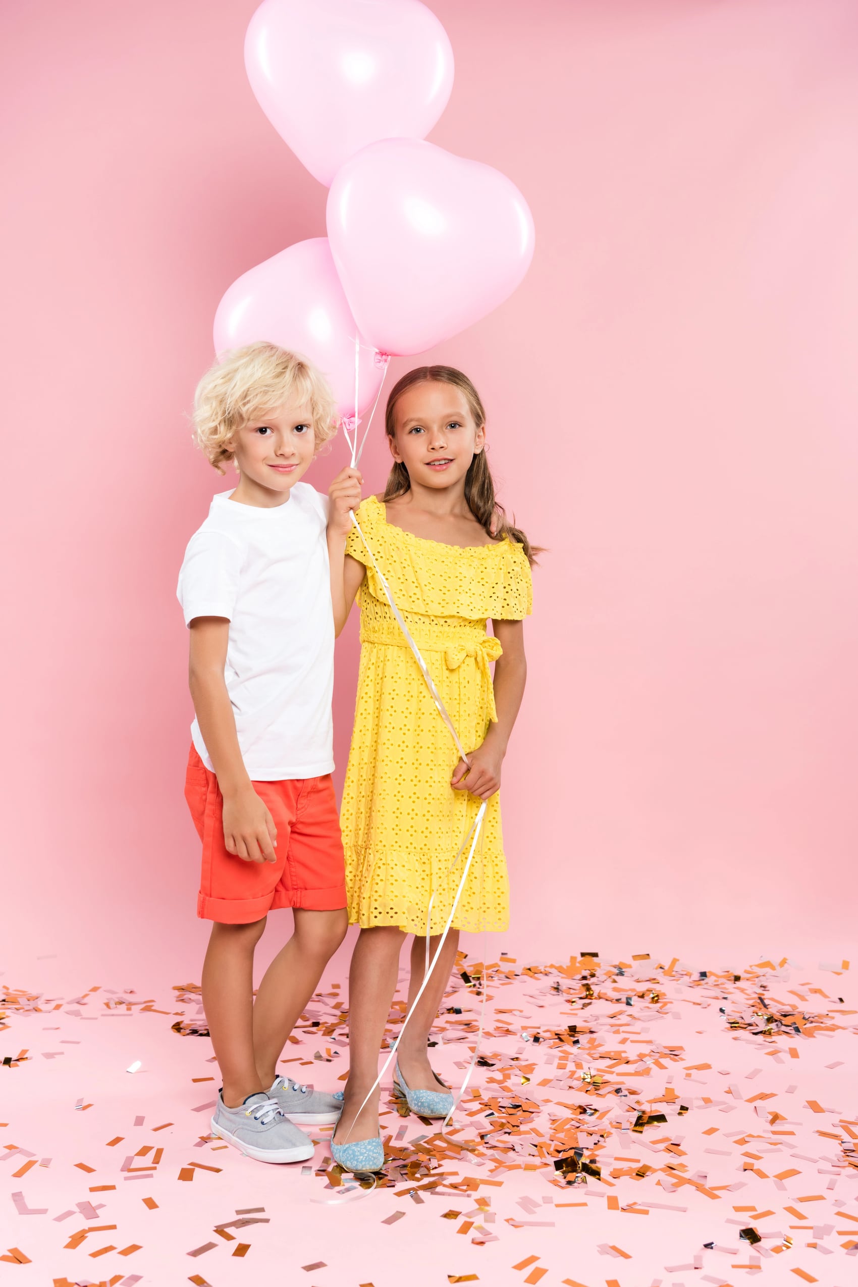 Mädchen im gelben Kleid und Junge mit Luftballons auf Party vor rosa Hintergrund