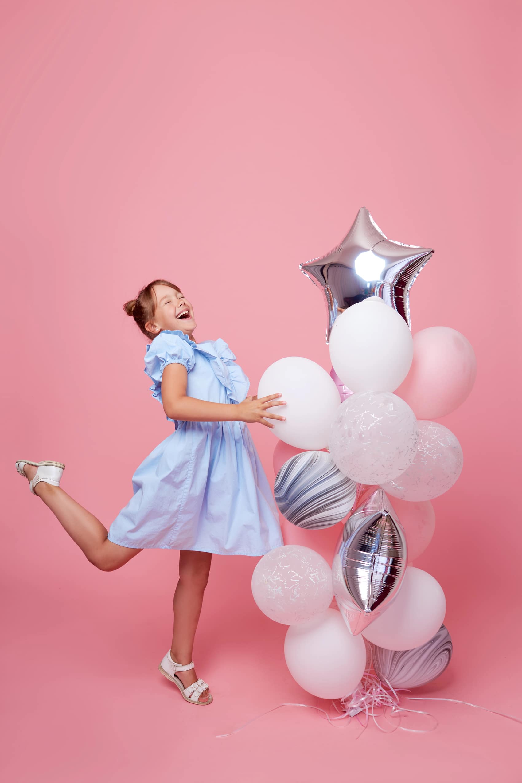 Mädchen im blauen Kleid lacht mit Luftballons vor rosa Hintergrund