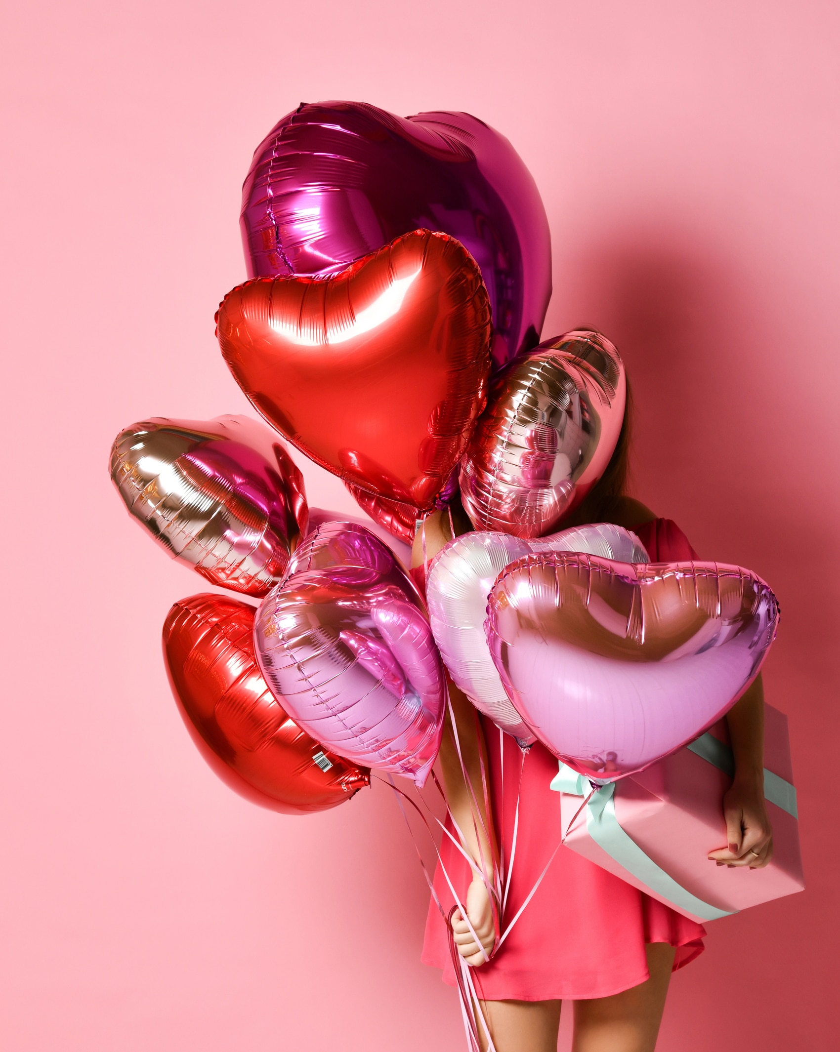 Mädchen hält Herzluftballons und Geschenk vor rosa Hintergrund