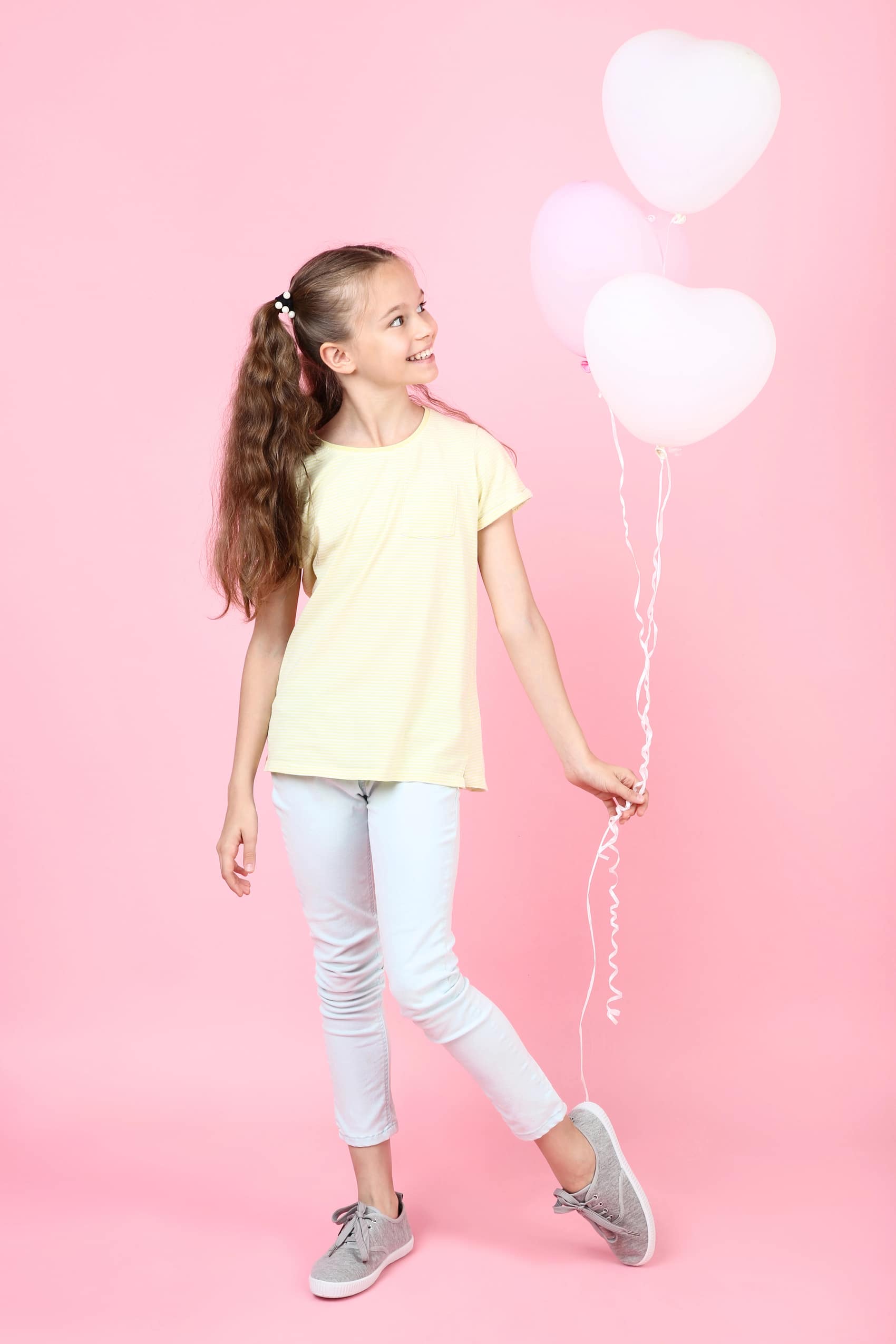 Mädchen hält rosa Herzluftballons vor rosa Hintergrund