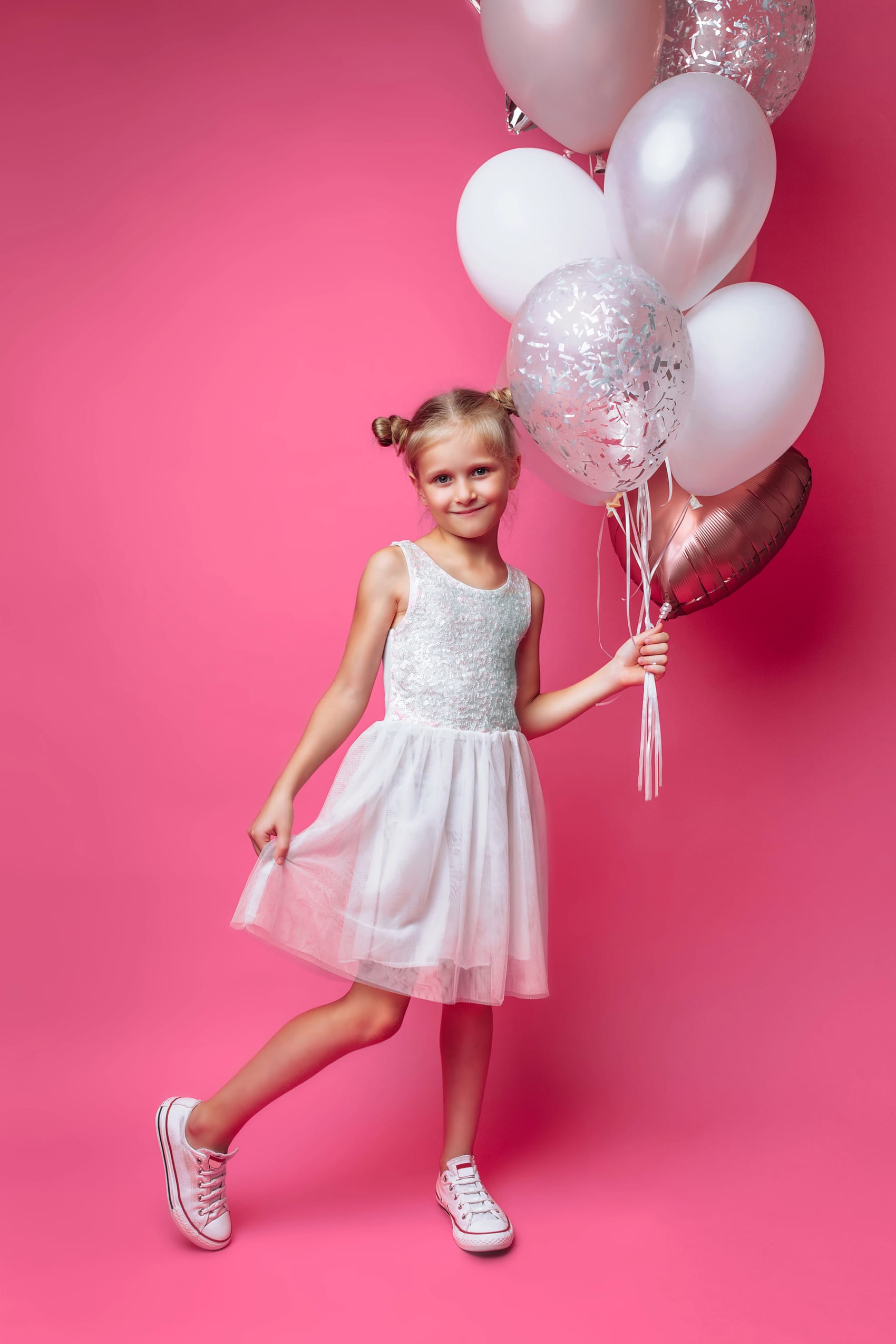 Mädchen im weißen Kleid mit Ballons vor rosa Hintergrund