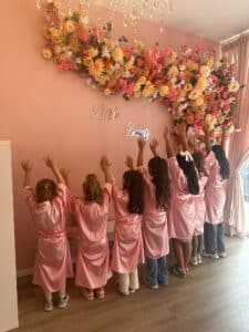Mädchen in rosa Bademänteln vor Blumenwand feiern Geburtstag