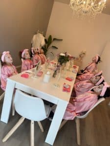 Mädchen in rosa Bademänteln mit Gesichtsmasken am Tisch