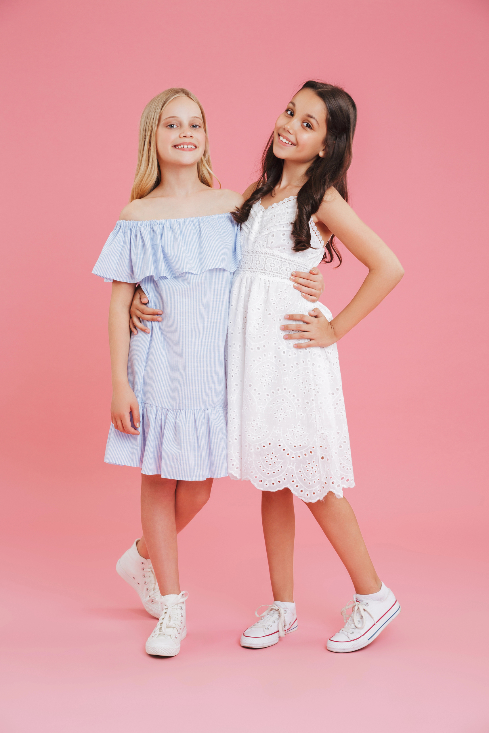Zwei Mädchen im Sommerkleid umarmen sich vor rosa Hintergrund